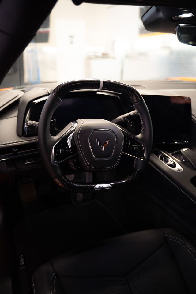 The interior cockpit of a modern sports car, focusing on its square-shaped steering wheel with the Corvette logo.