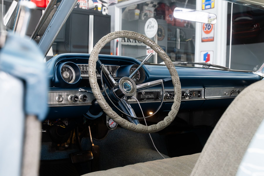 Interior view of a vintage blue car, featuring a textured steering wheel cover and a classic dashboard in a garage.