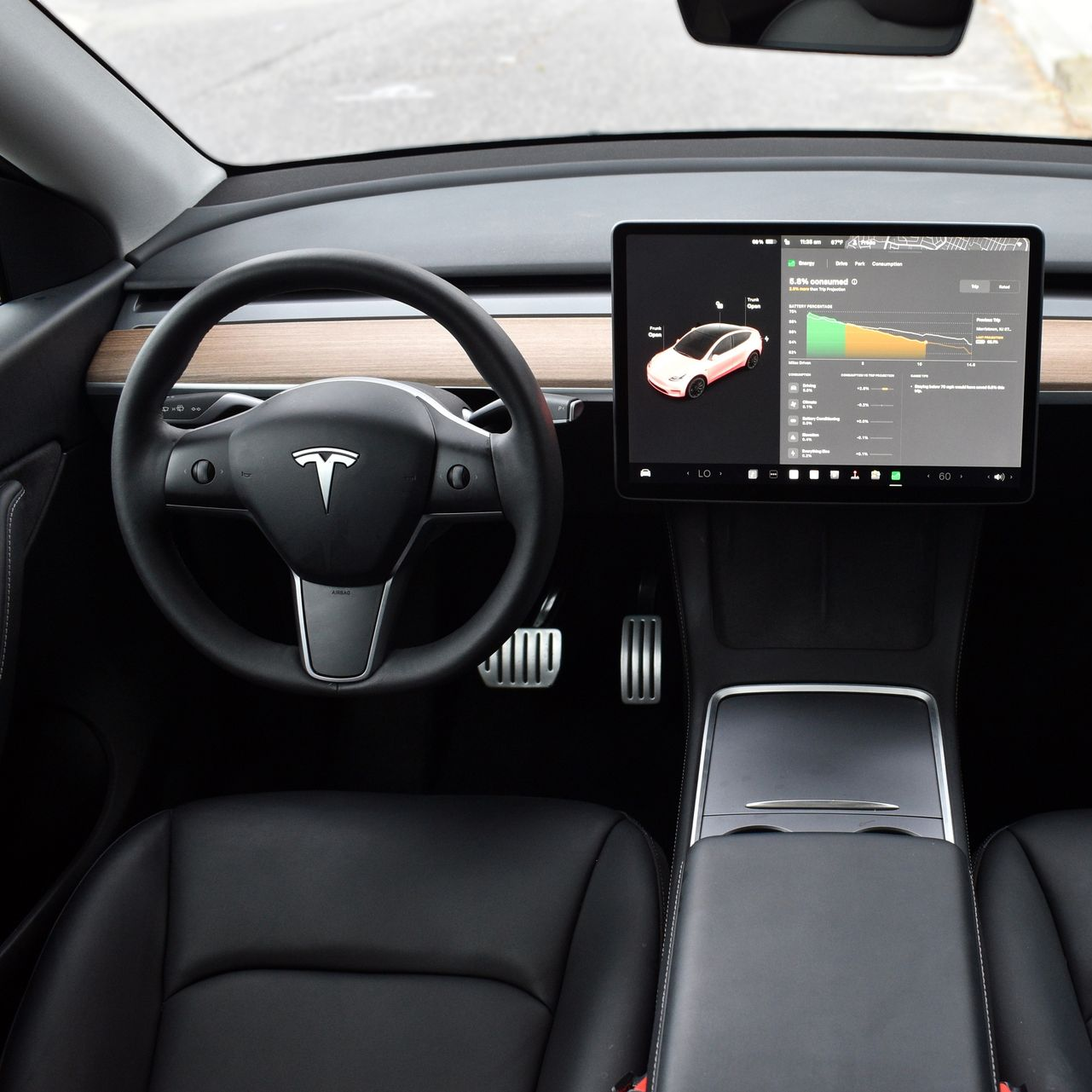 The interior of a Tesla with a minimalist dashboard, steering wheel, and a large touchscreen display showing energy data.
