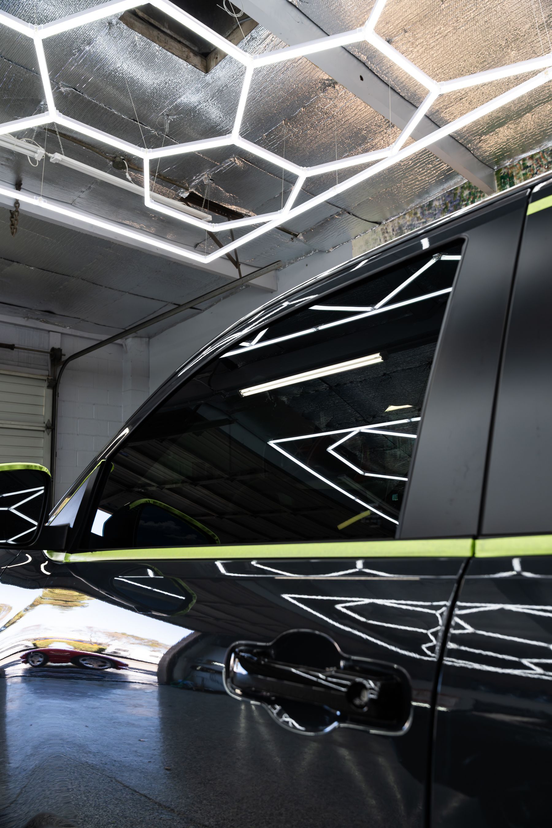 A close-up of a black car door with a bright green trim accent under modern geometric hexagonal overhead lighting.