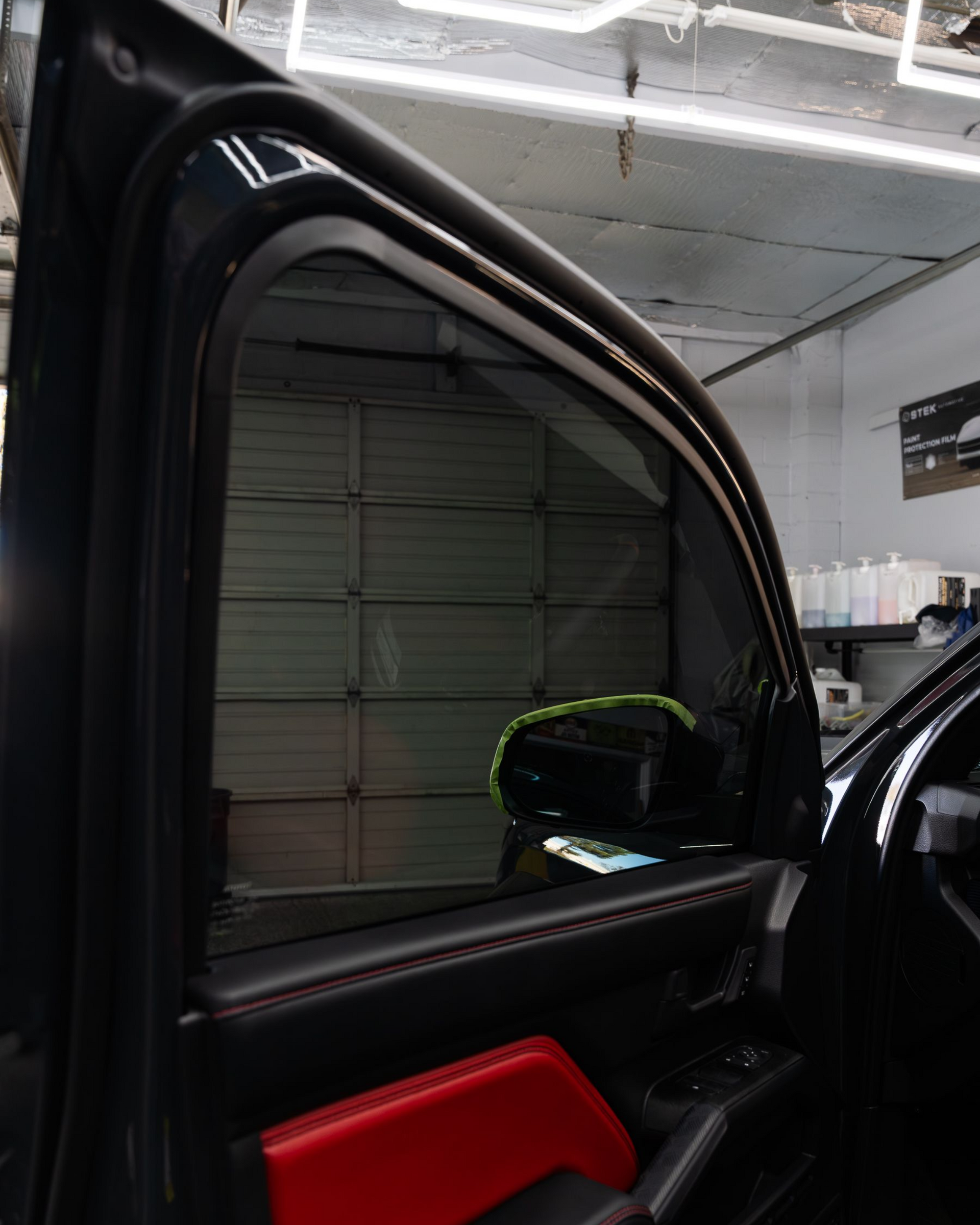 A black Ford Mustang with a rear spoiler, black wheels, and visible red brake calipers parked on pavement.