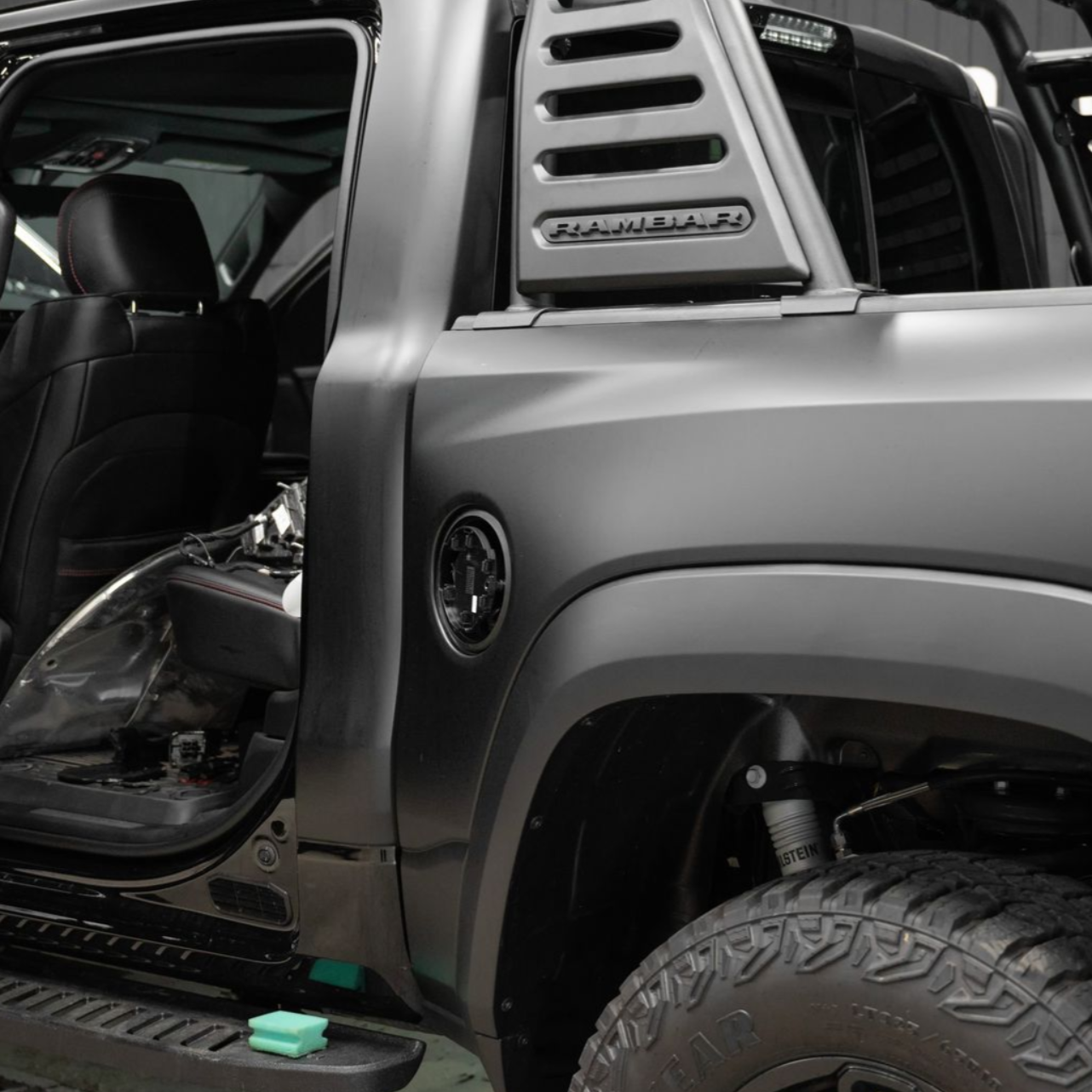 A matte black truck with an open door and a louvered sport bar on its bed, shown from a rear three-quarter view.