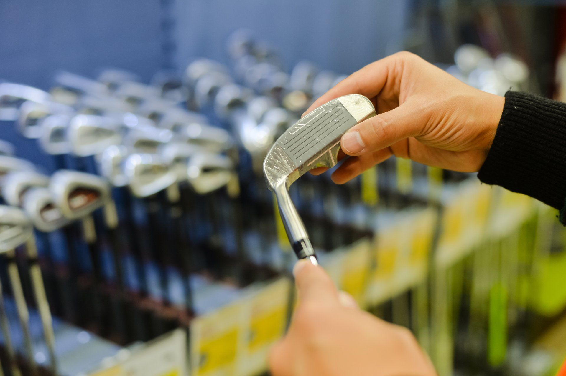 Person holding in hand club at a golf shop. Closeup photo of choice concept.