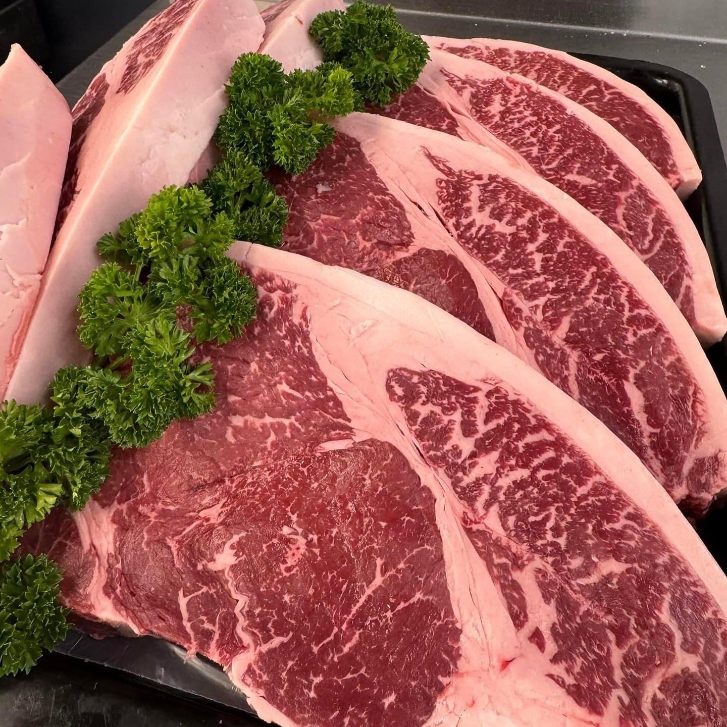 Close-up of several raw, marbled steaks arranged on a tray, garnished with green parsley.