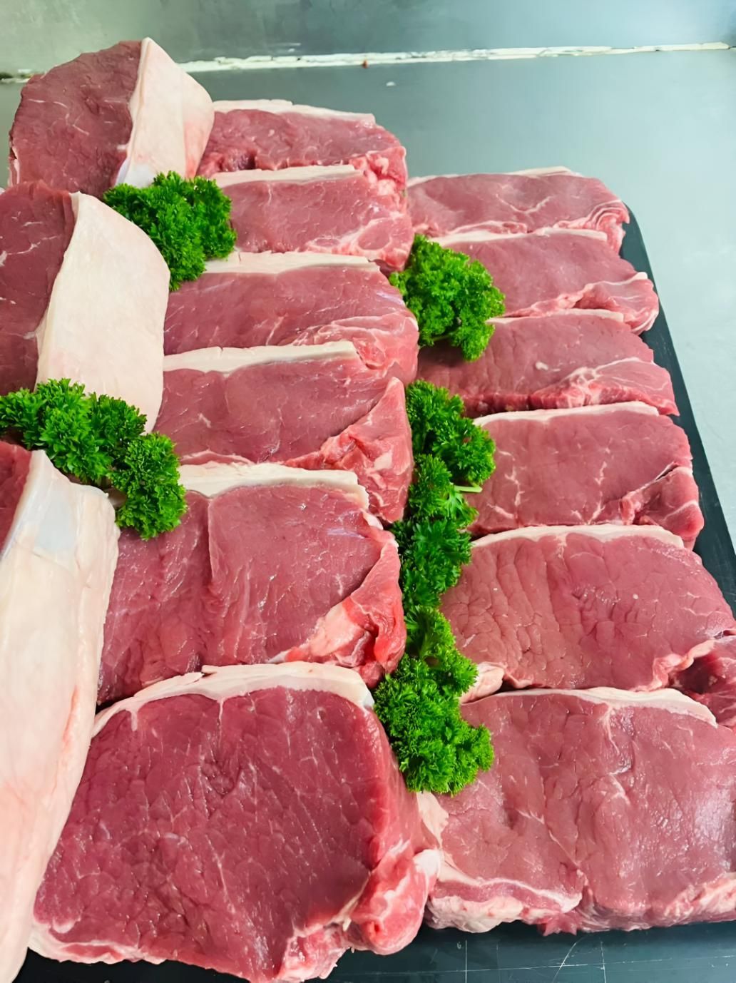 A Tray of Raw Steaks With Parsley on Top — MBW Wholesale & Bulk In Cannonvale, QLD