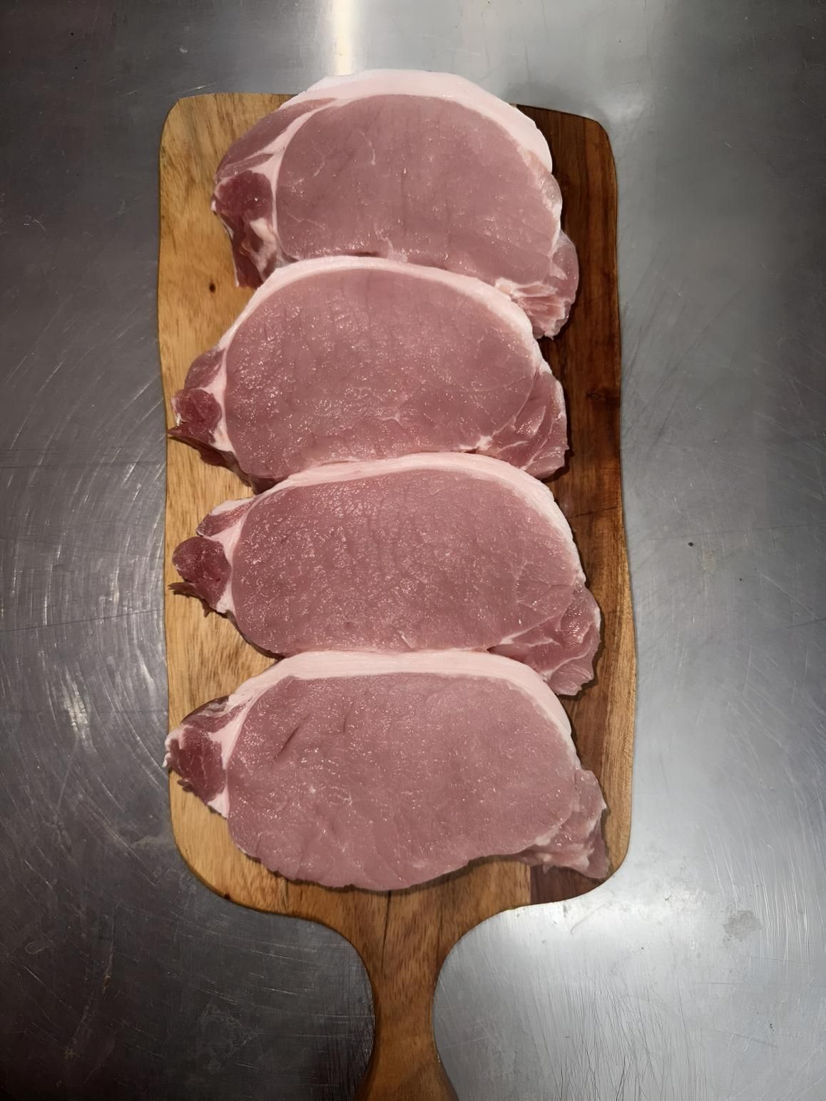Four Pork Chops Are Sitting on a Wooden Cutting Board — MBW Wholesale & Bulk In Cannonvale, QLD