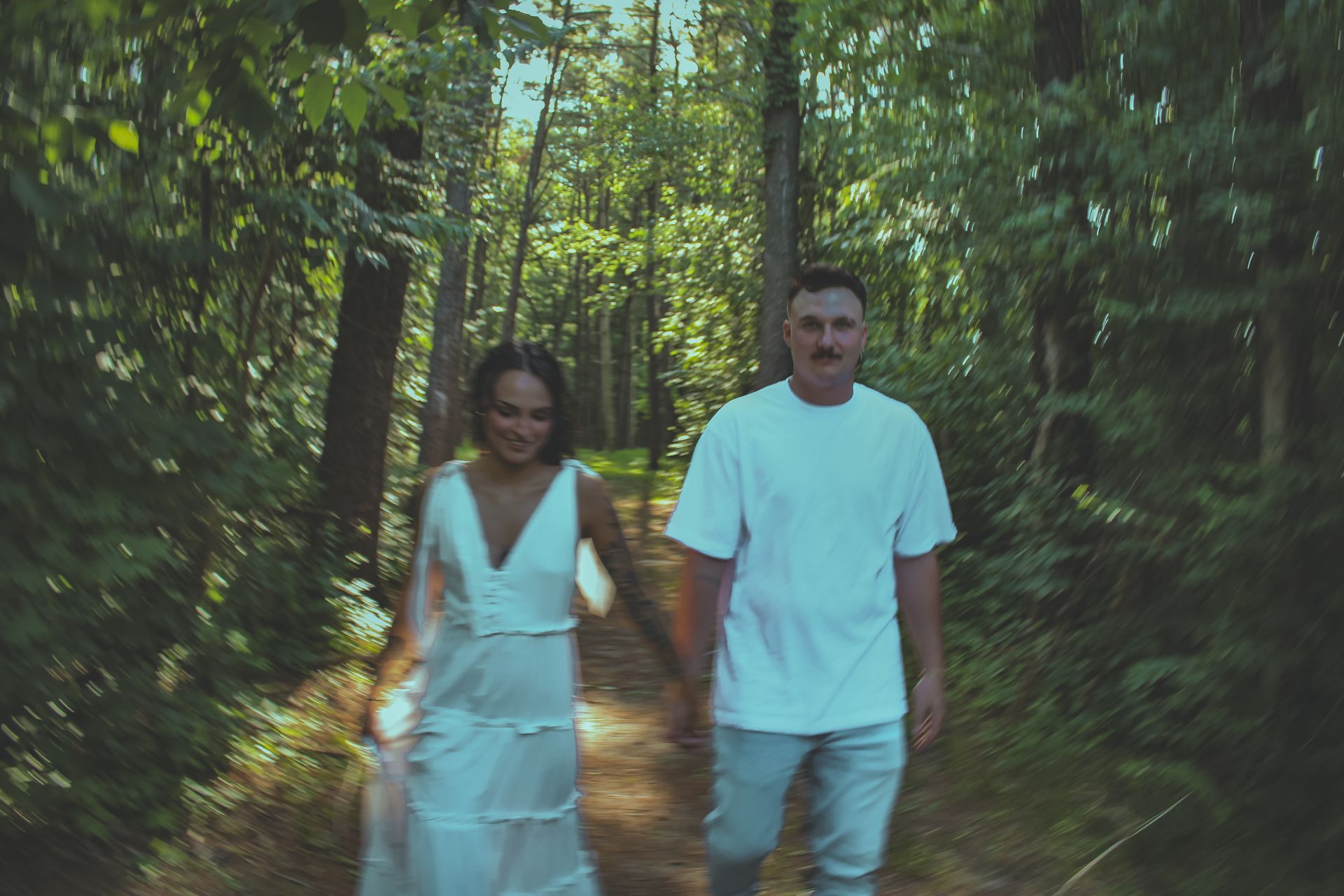 A man and a woman are walking down a path in the woods holding hands.