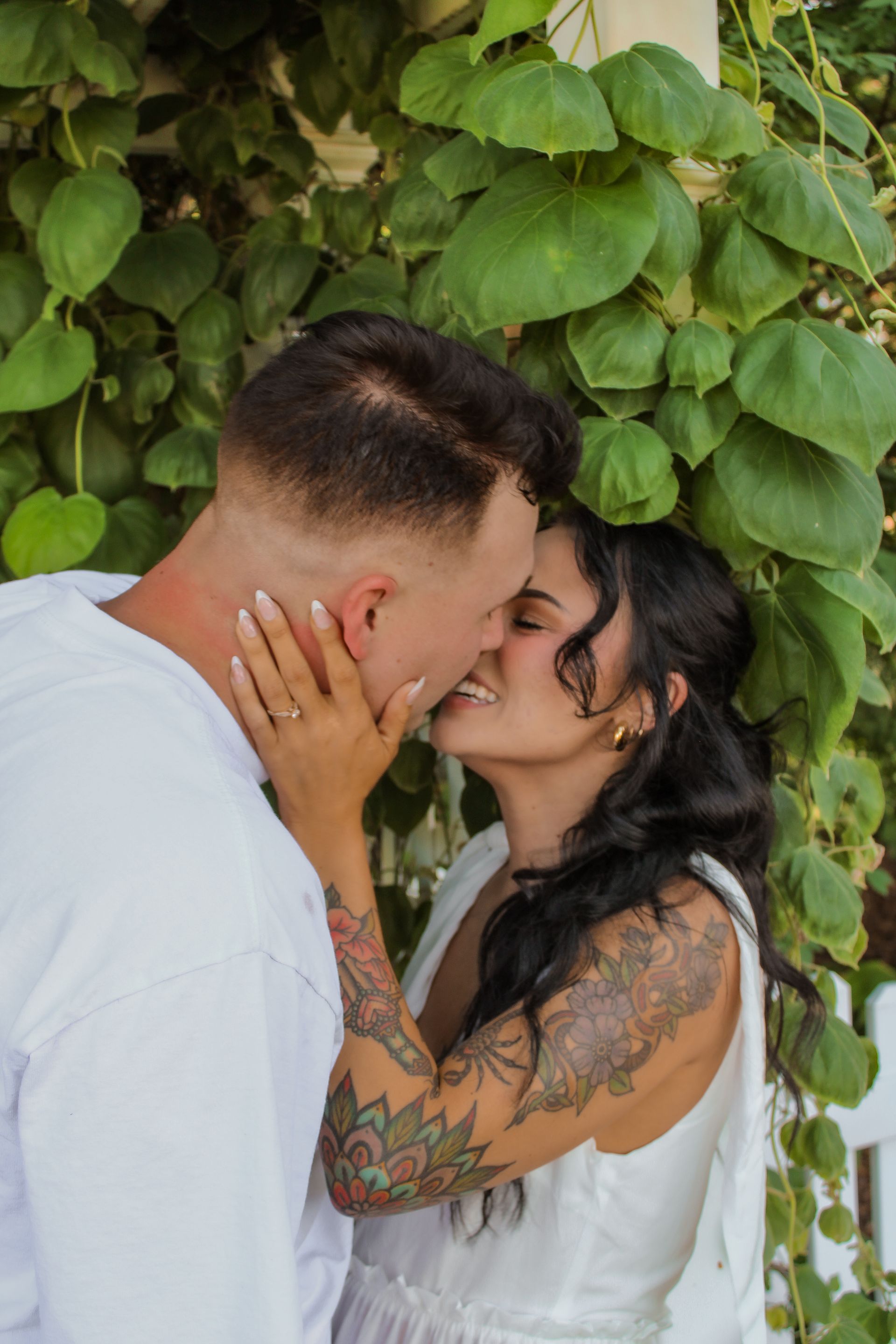 A man and a woman are kissing in front of a bush.
