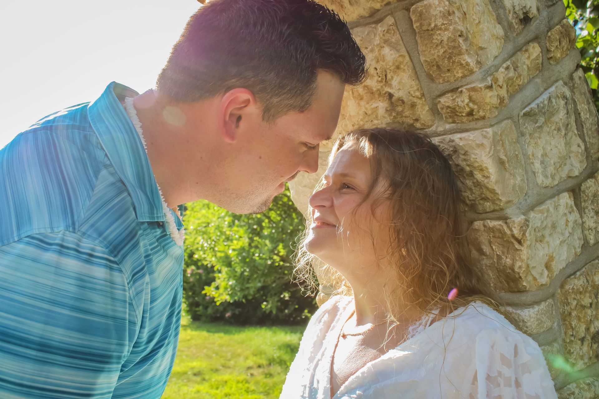 Couple gazing at each other lovingly, leaning against a stone structure outdoors.
