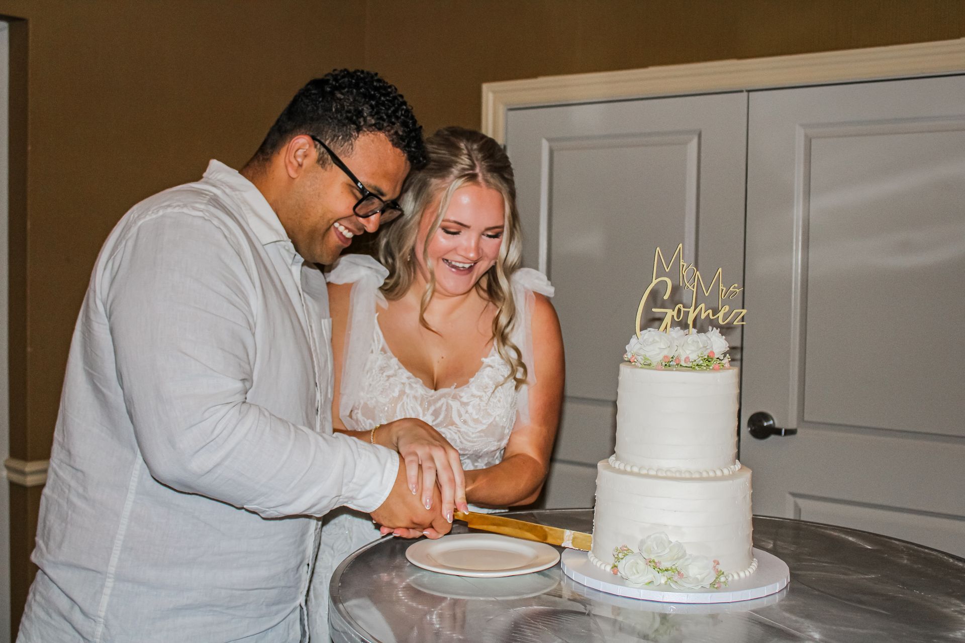 Couple smiling, cutting a tiered wedding cake with 