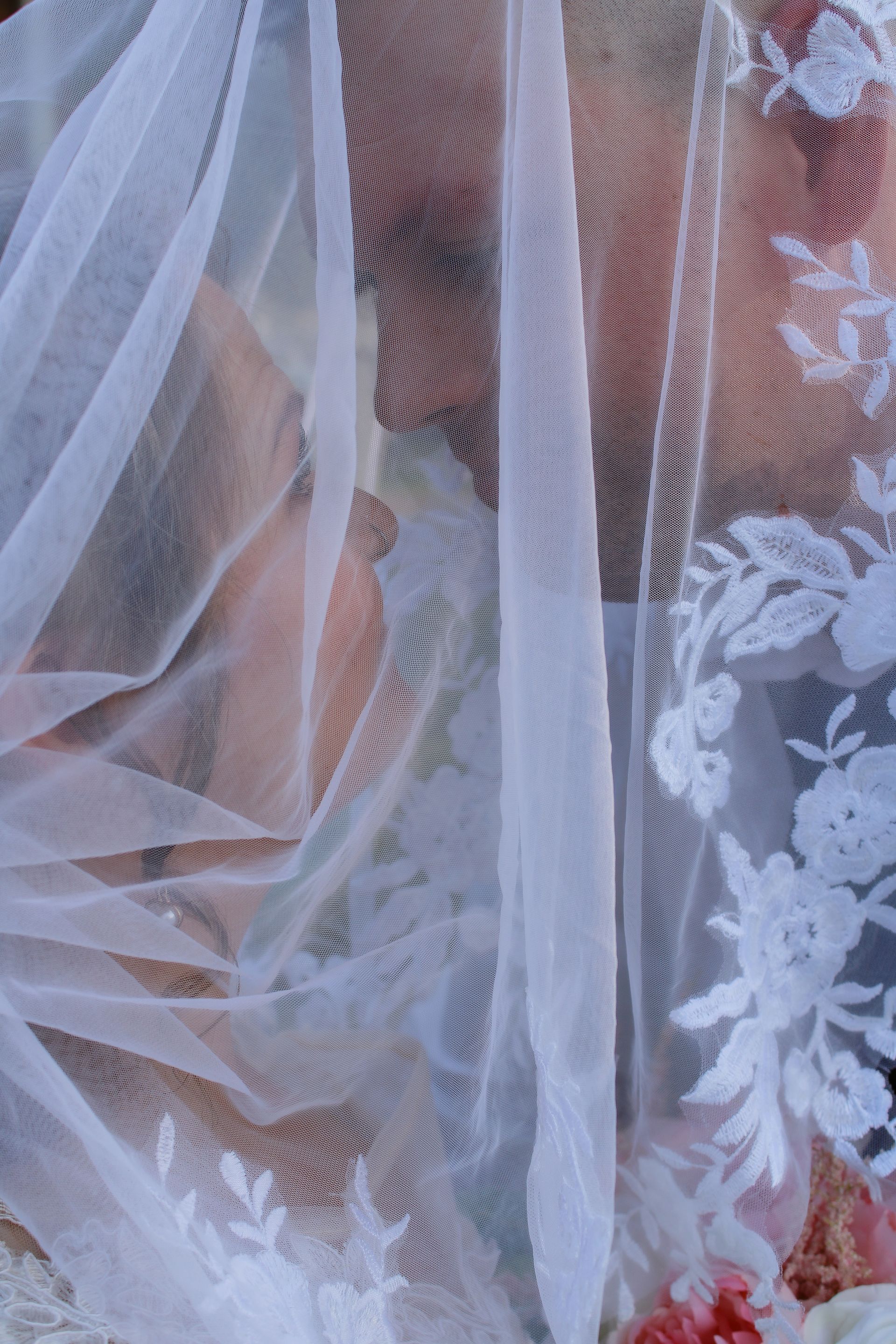 White lace veil, delicate floral detailing, draping over a person, blurred background.