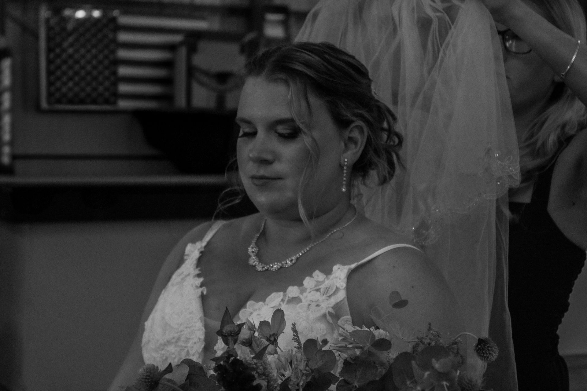 Bride getting her veil adjusted; she's wearing a white dress, holding flowers, and has a tattoo.