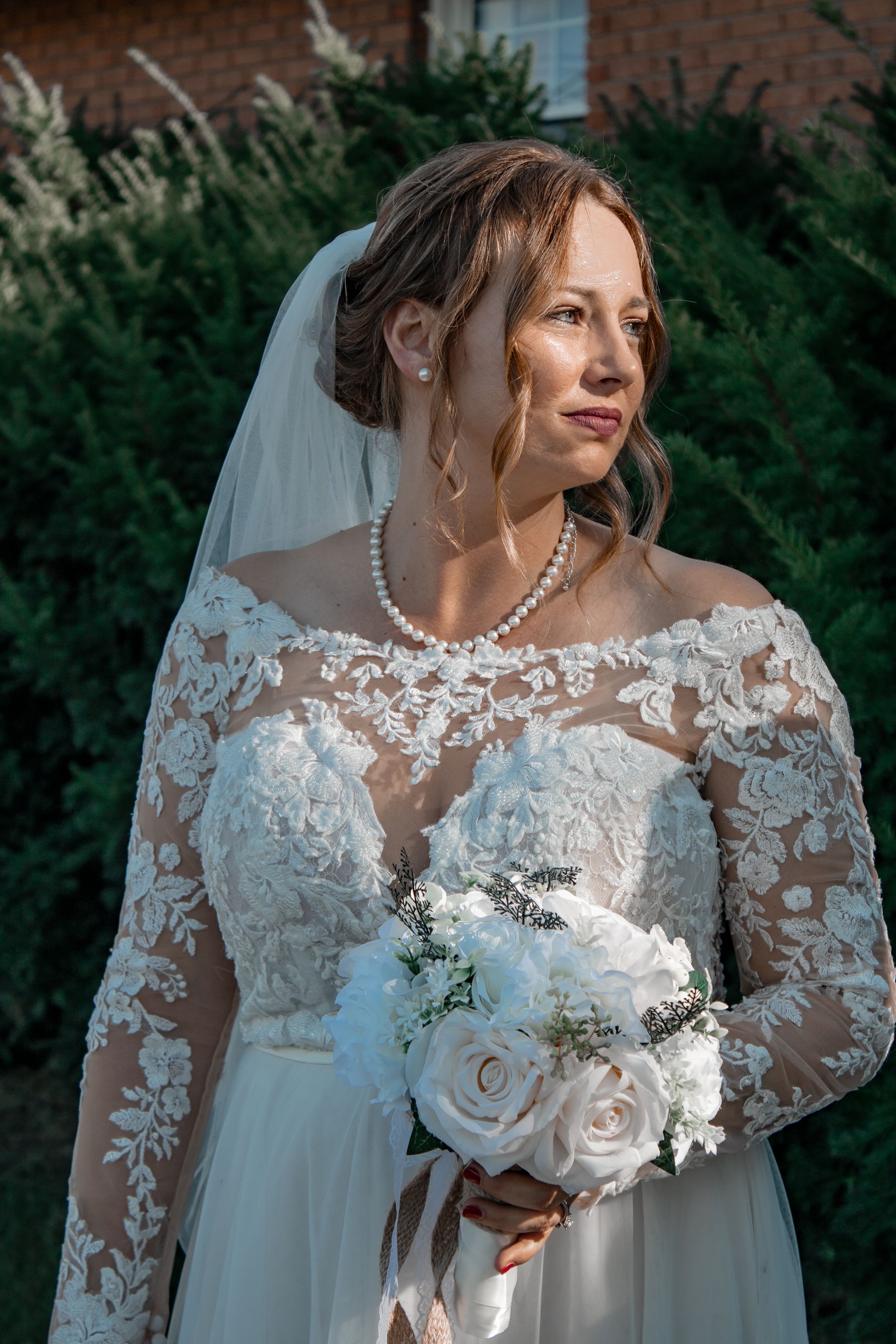 Bride in a lace wedding dress, holding a bouquet, looking to the side.