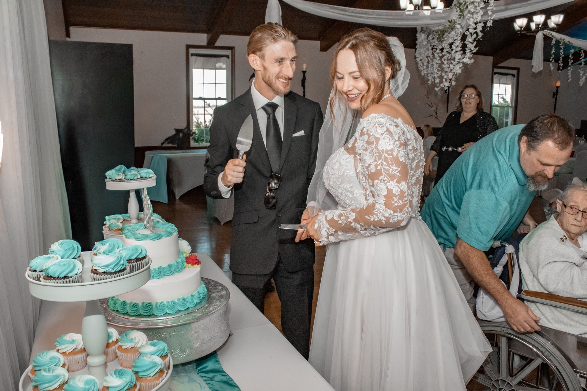 Bride and groom cutting wedding cake at reception, guests watching.
