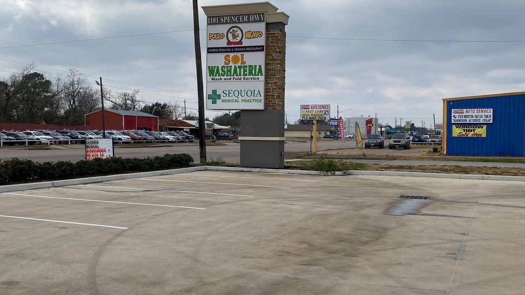 Shopping center with sign listing businesses, parking lot, overcast sky.