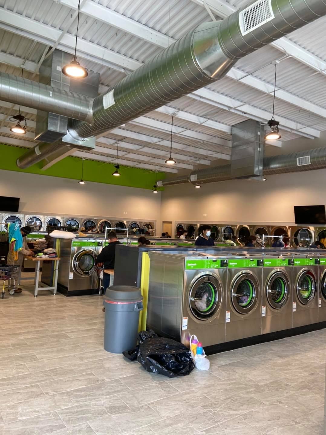 Interior of a laundromat with rows of washers and dryers. A person is sitting in front of a machine.