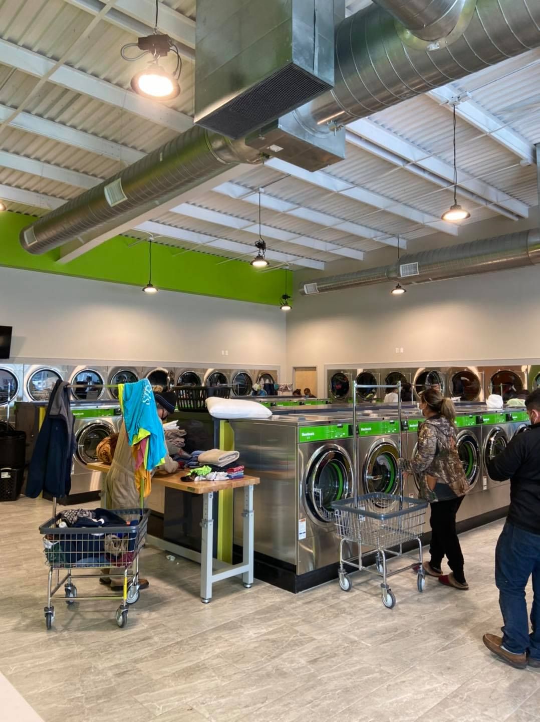 A brightly lit laundromat with washing machines. People do laundry.