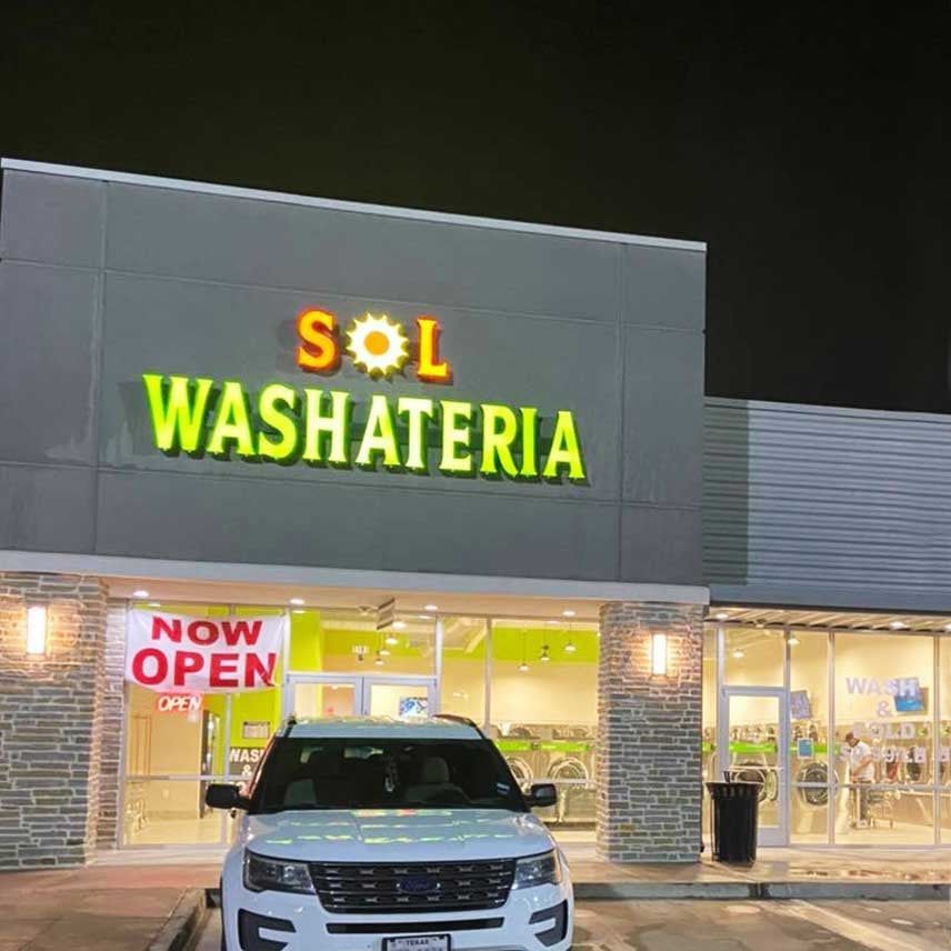 Exterior of Sol Washateria, a laundromat with a lit sign. A white SUV is parked in front, with 