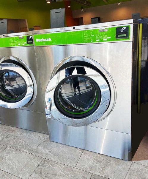 Two large, shiny, commercial washing machines with green accents in a laundromat.