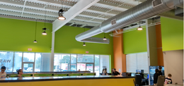 Interior with a yellow counter, green walls, and people seated. Metal air ducts run along the ceiling.