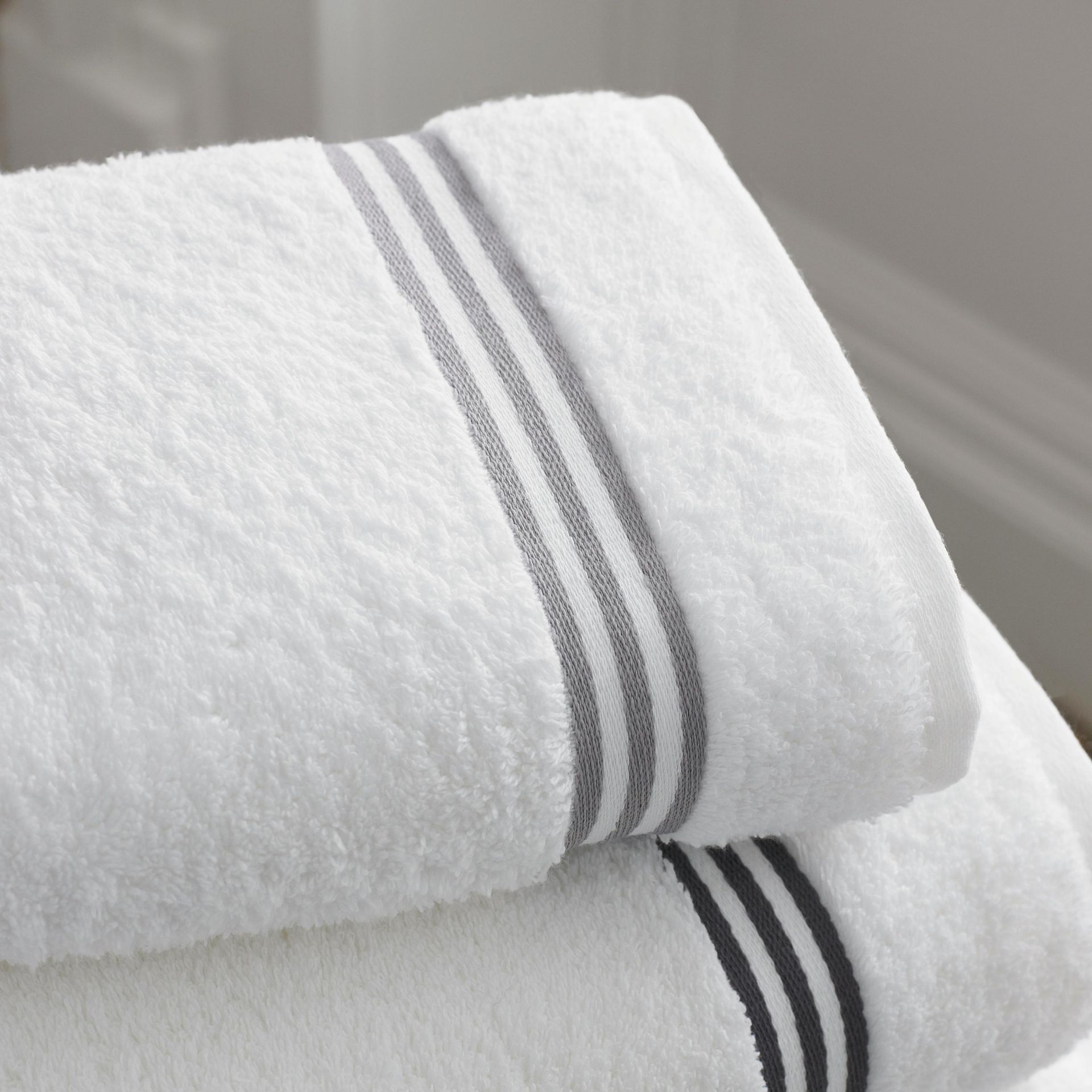 White bath towels folded, with gray stripes at the hems.