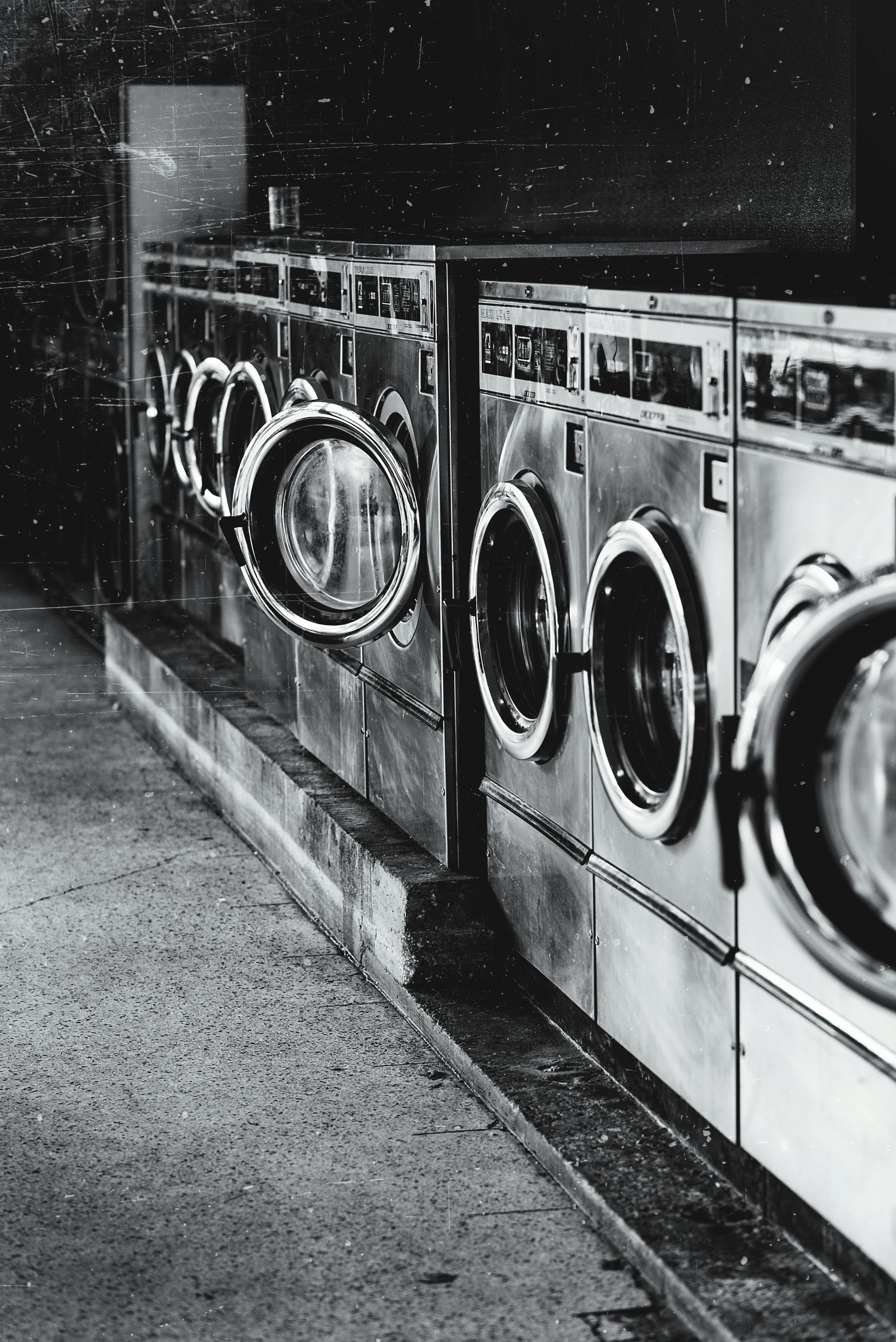 Row of washing machines in a laundromat, mostly in shadow. Doors are circular and glass.