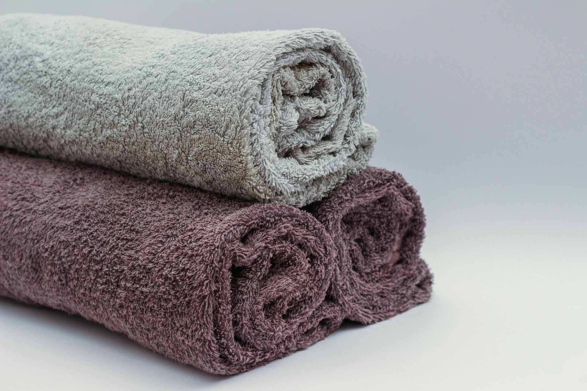 Three rolled towels: gray, mauve, and purple stacked on a white surface.
