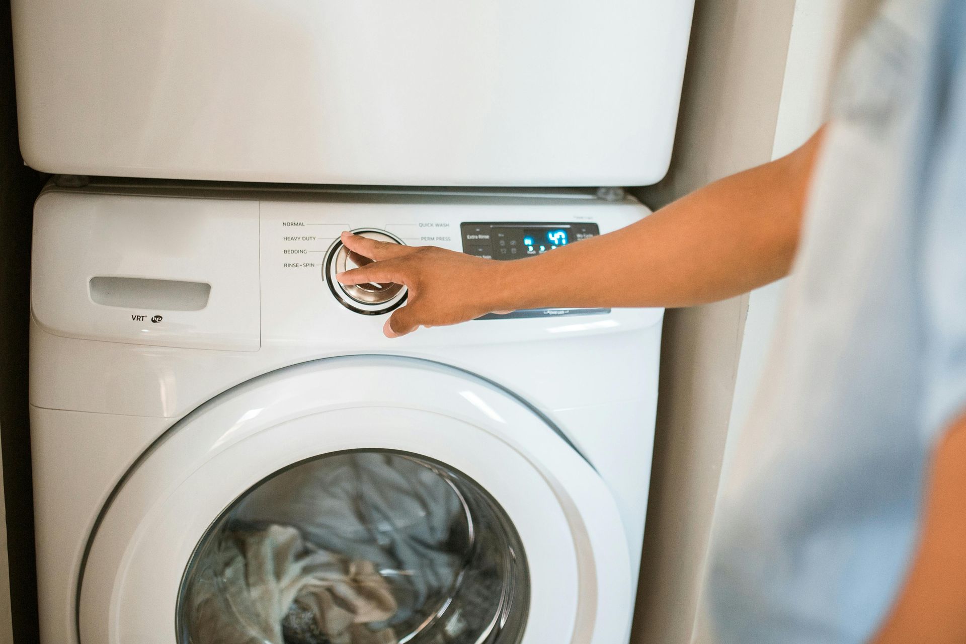 Person turning dial on white washing machine.