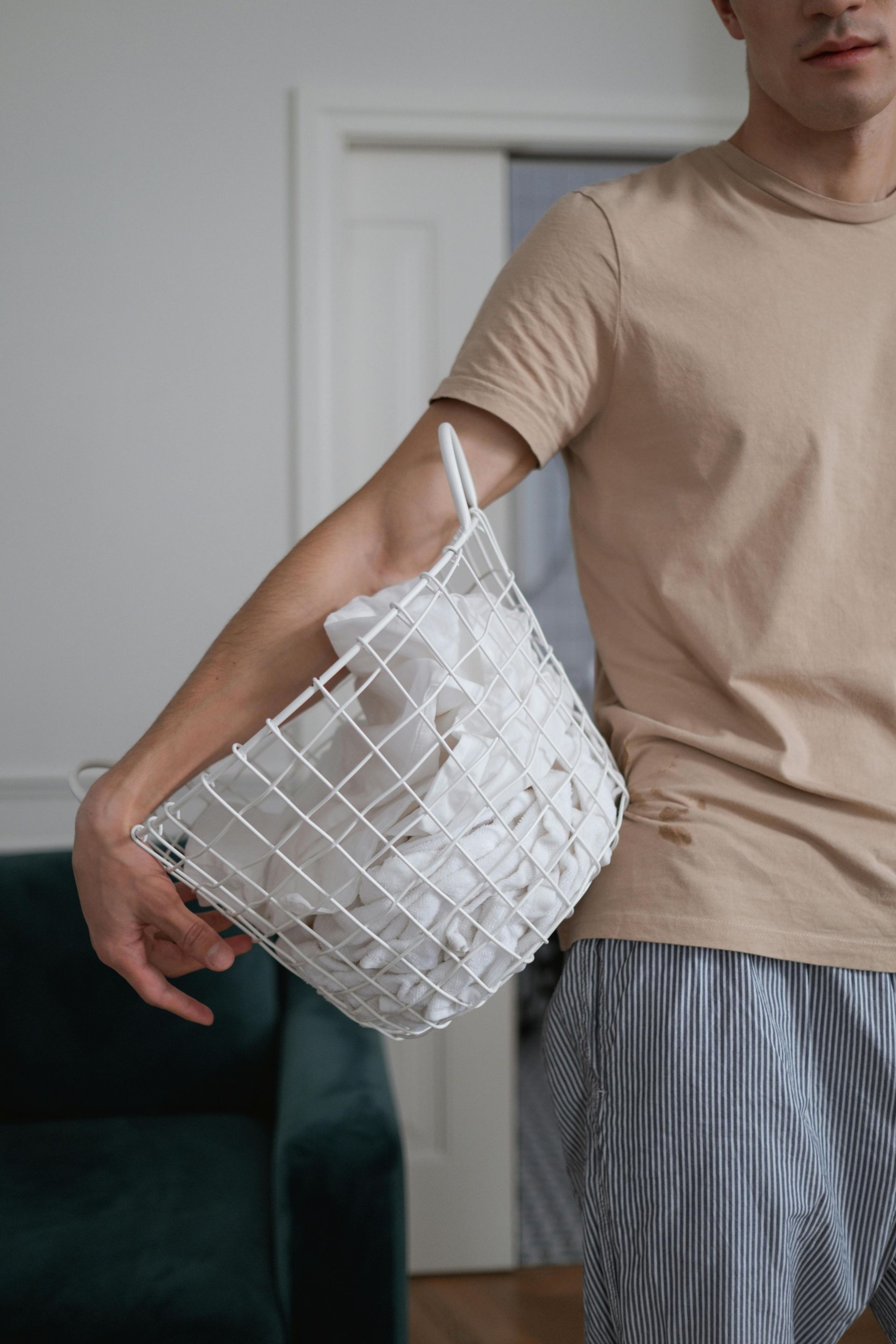 Person carrying a white wire basket filled with folded white linens.