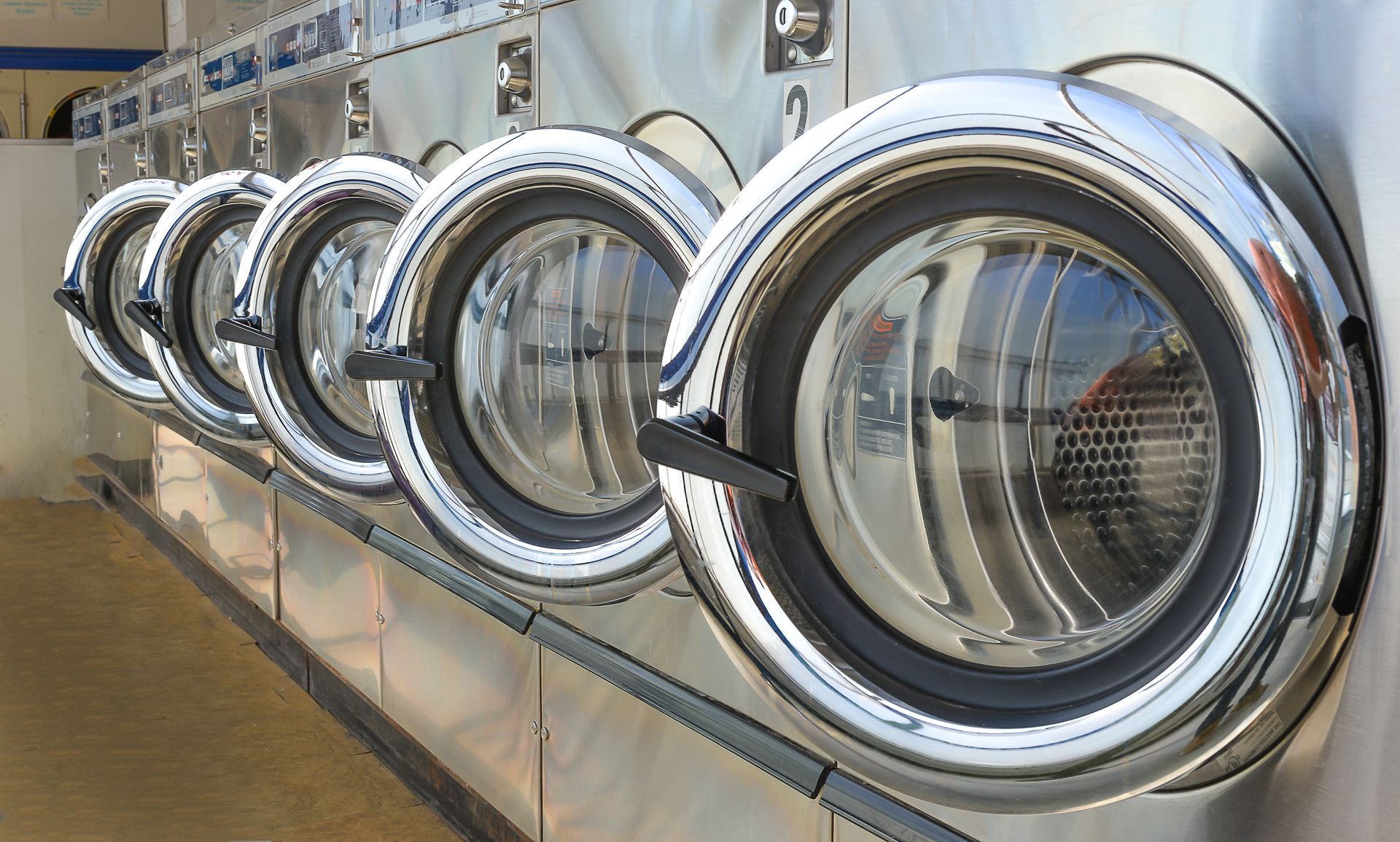 Row of industrial front-loading washing machines in a laundromat, stainless steel and chrome.