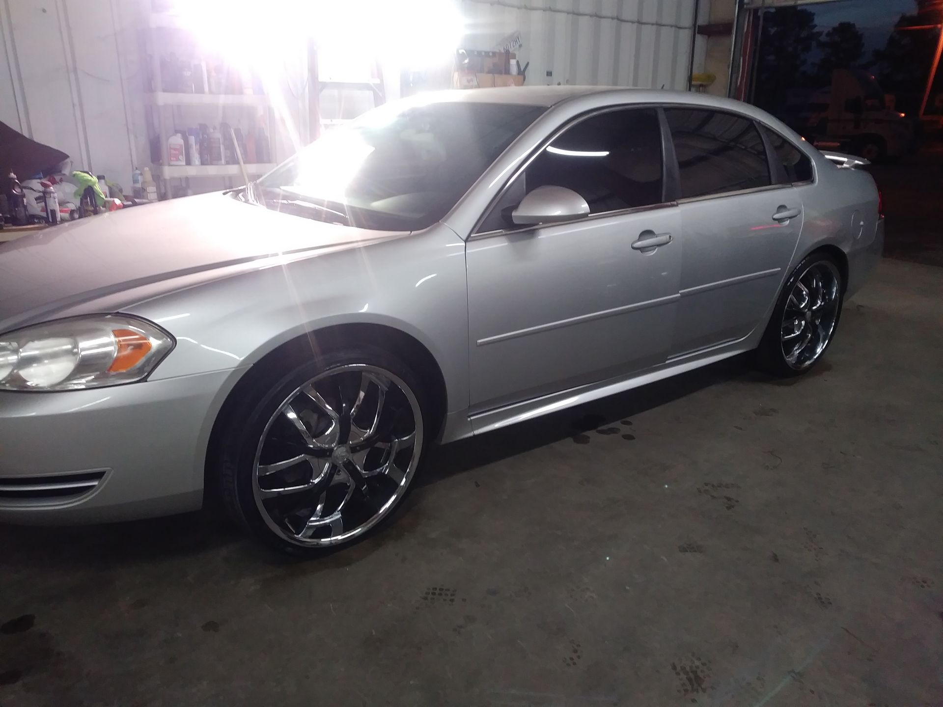 Silver Chevrolet Impala with custom black and chrome rims parked indoors.