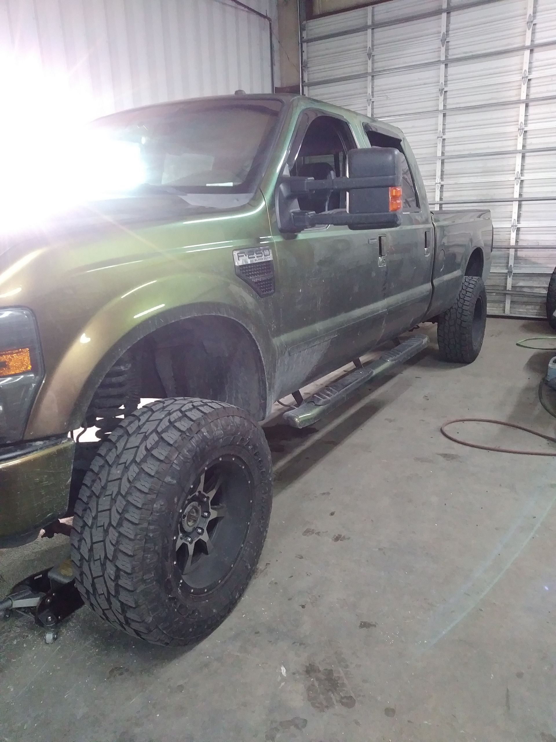 Green lifted pickup truck in a garage, with large tires and running boards.