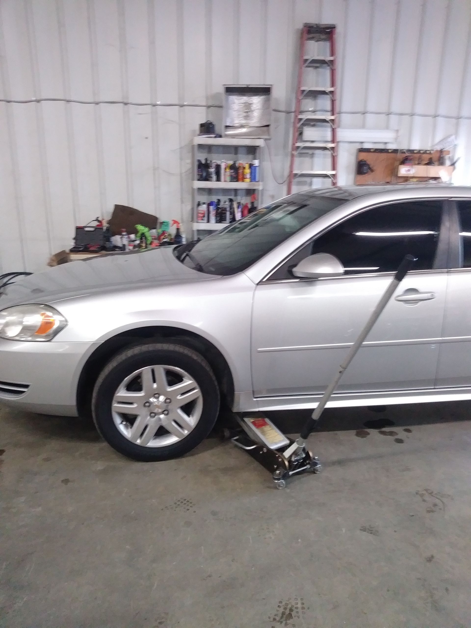 Silver car lifted by a jack in a garage, presumably for tire work.