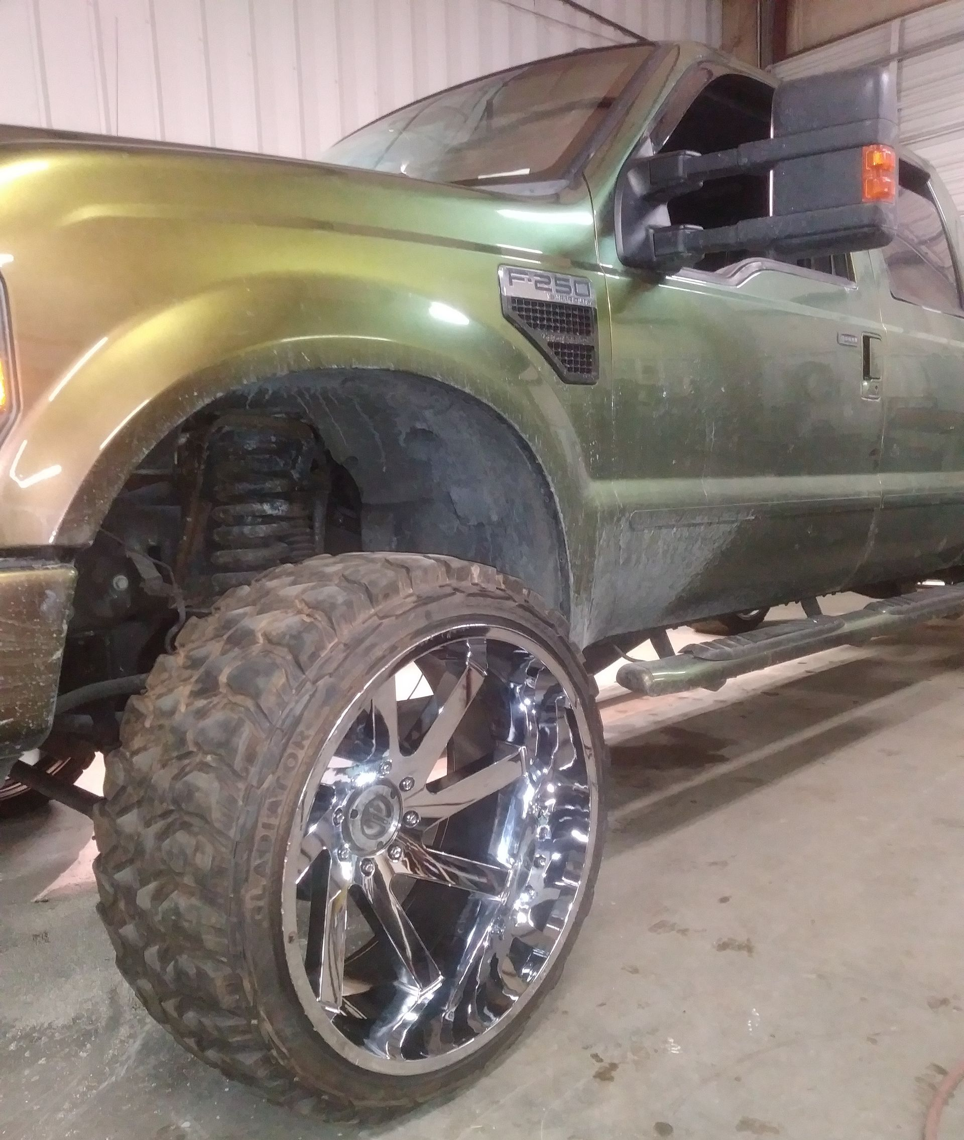 Green lifted truck with chrome rims and large tires.