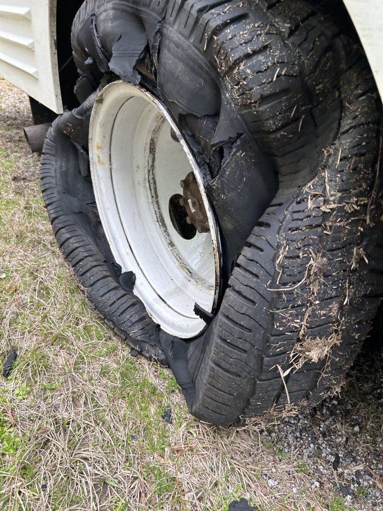 Destroyed tire on a white rim, flat on the ground. The tire is torn with rubber debris scattered around.