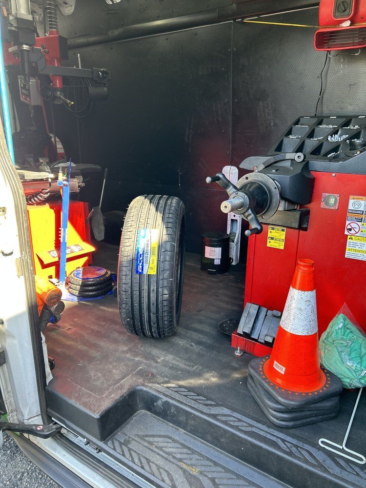 Inside of a van, a tire stands next to tire balancing equipment. Orange cone on the right.