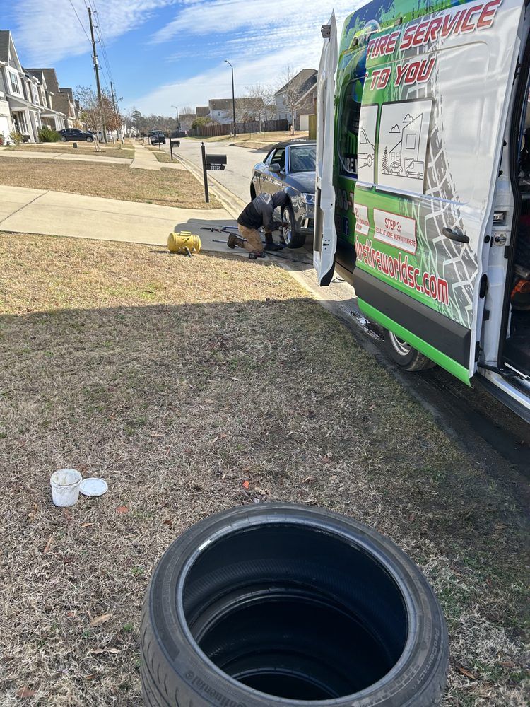 Mechanic changing a tire next to a service van on a residential street, sunny day.