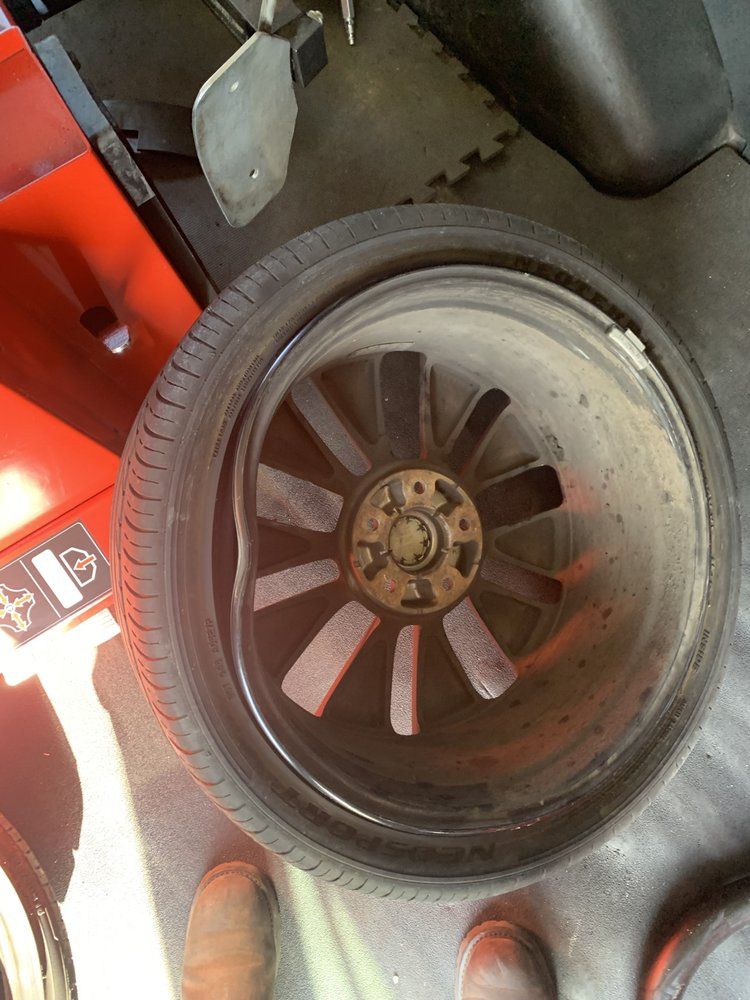 Bent black car wheel with a tire, sitting in a garage.