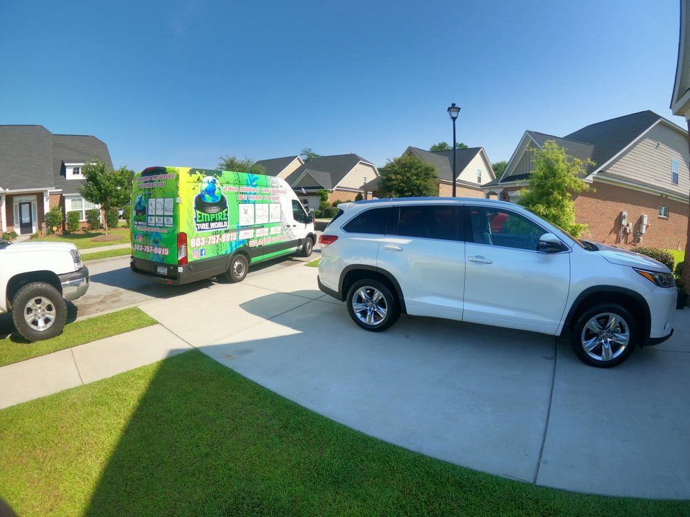 Vehicles parked in a residential driveway on a sunny day. A van, SUV and truck are present.
