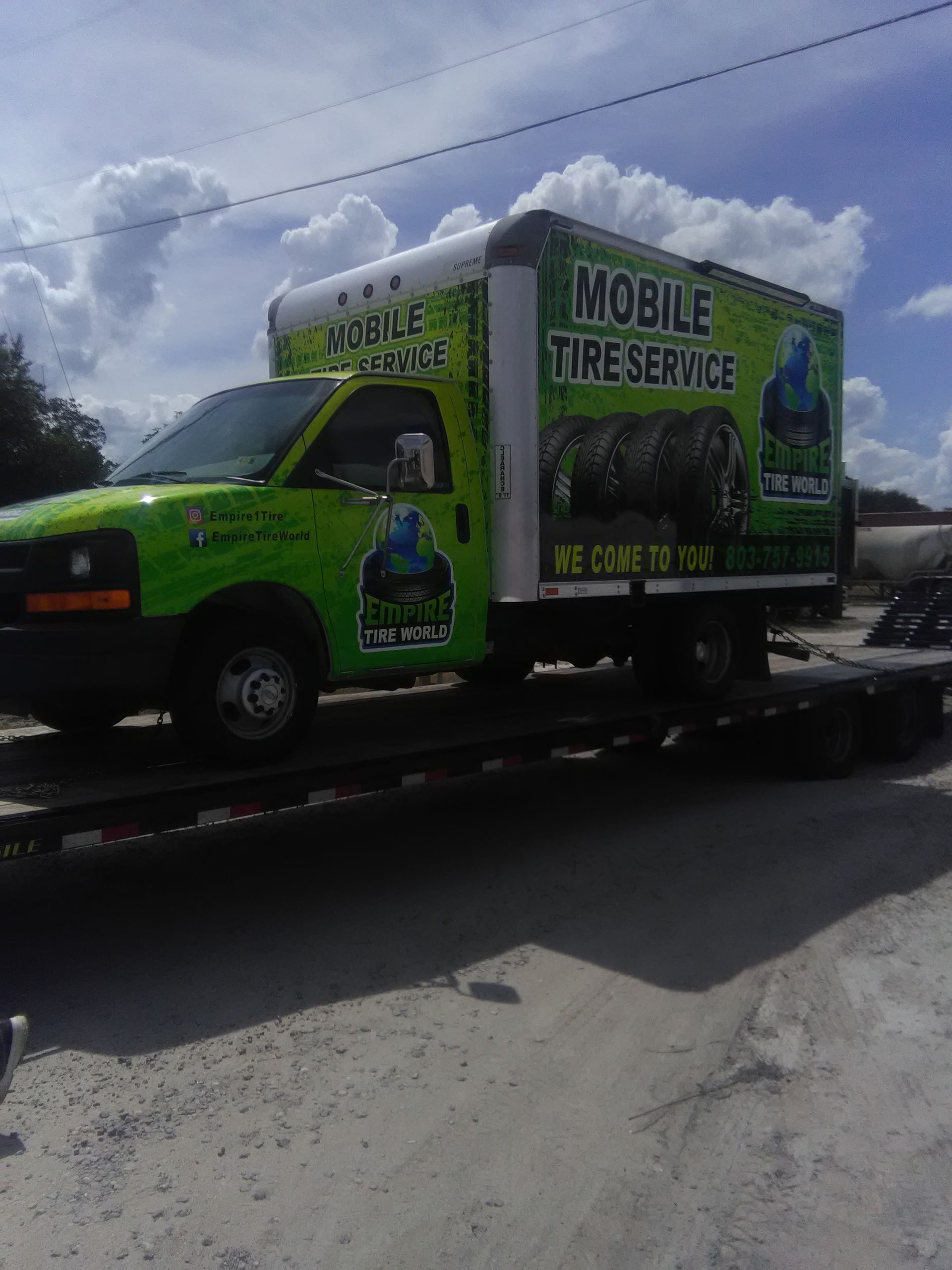 Green and white mobile tire service truck on a trailer, under a cloudy sky.