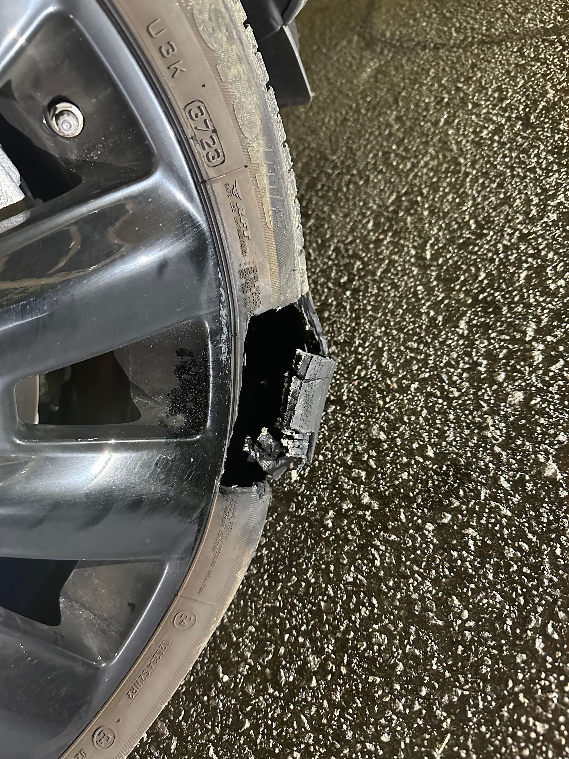 Damaged black car wheel with a chunk missing; tire visible; asphalt background.