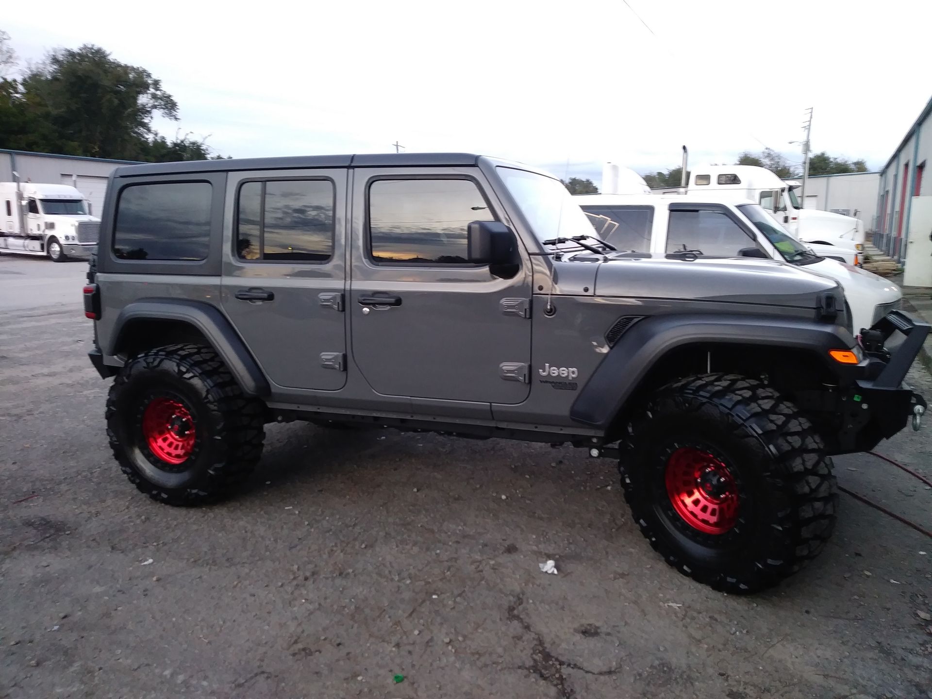 Gray Jeep Wrangler with large black tires and red rims parked outside.
