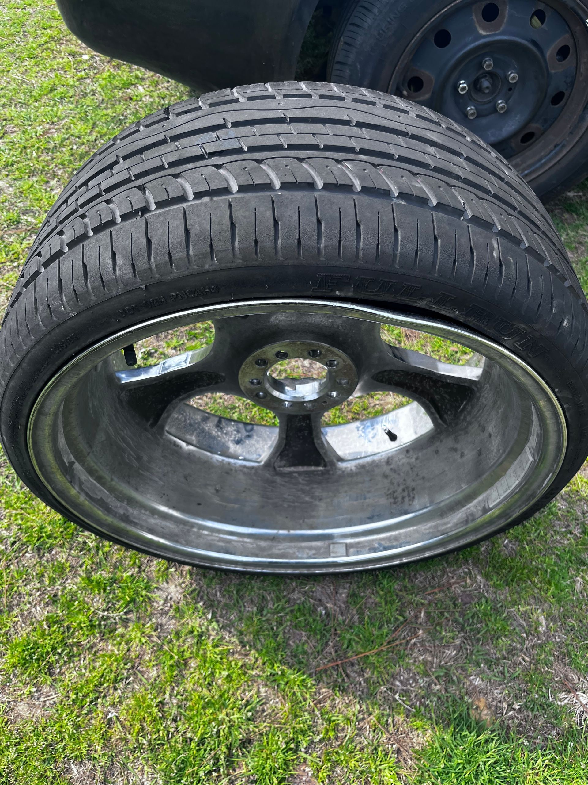 Chrome car wheel with worn tire on grass.