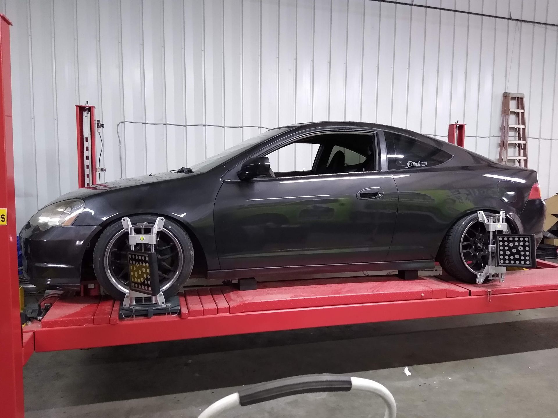Gray car on a lift being aligned in a garage.