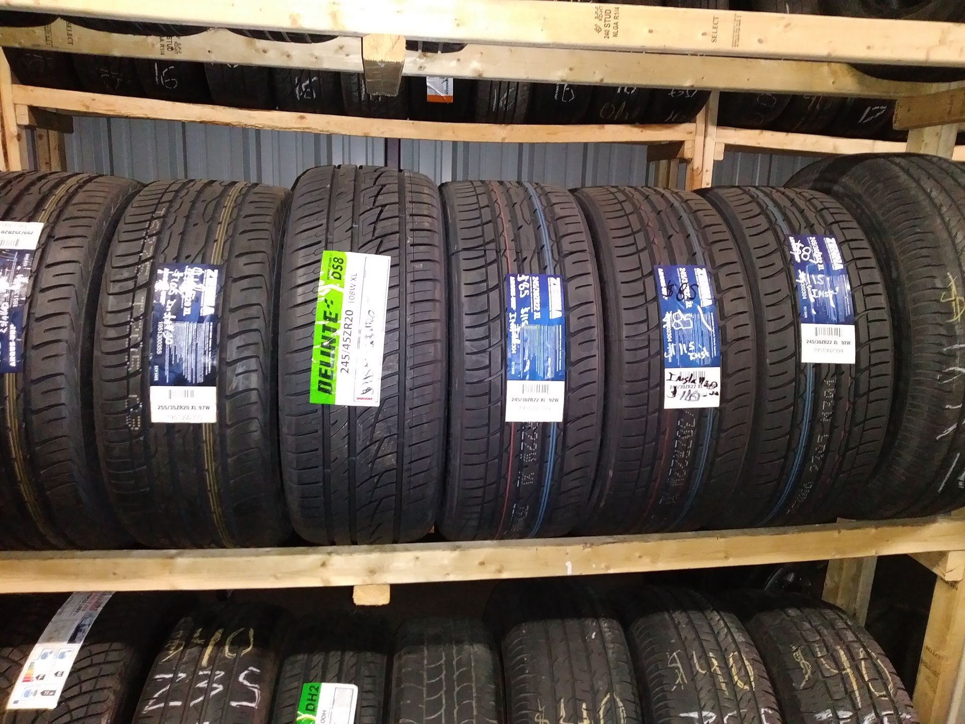 Tires stacked on wooden shelves in a warehouse; black rubber with various labels visible.