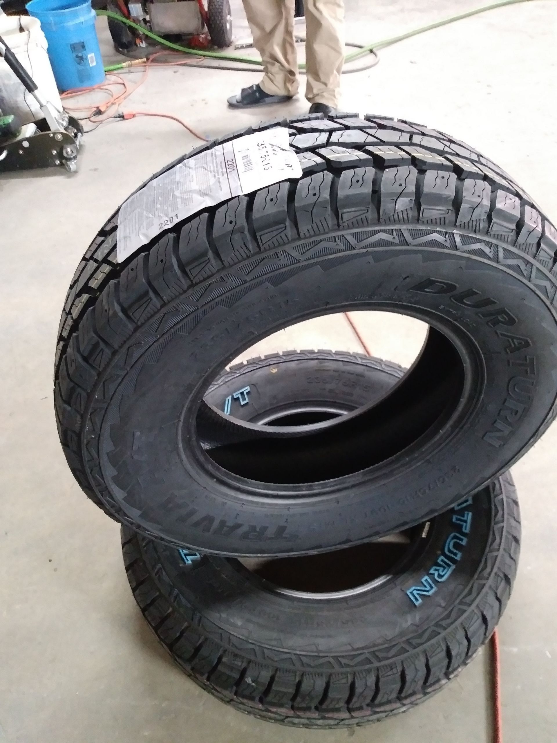 Three new black truck tires stacked, ready for mounting in a garage.