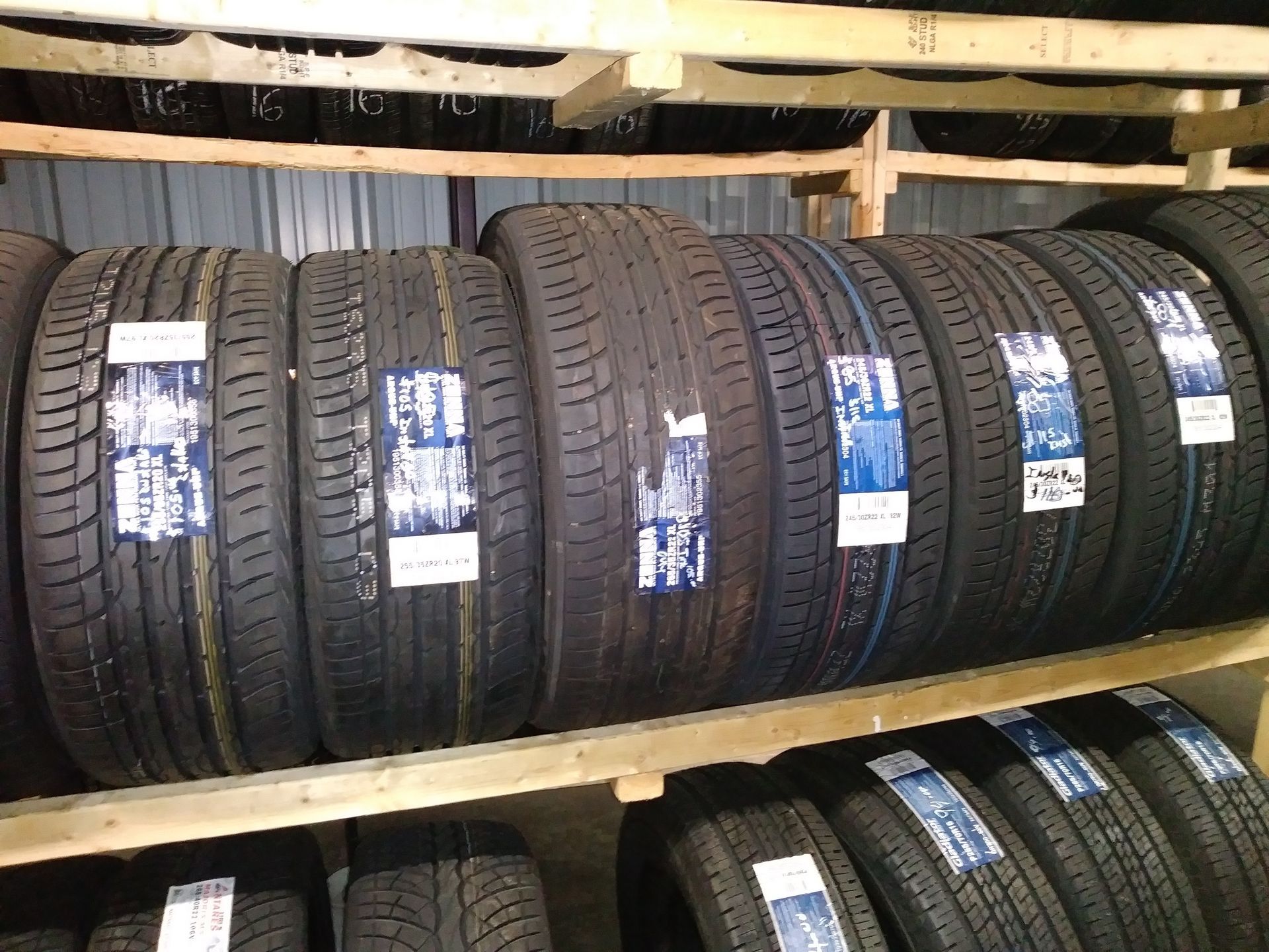 Tires stacked on wooden shelves in a warehouse setting, ready for sale.