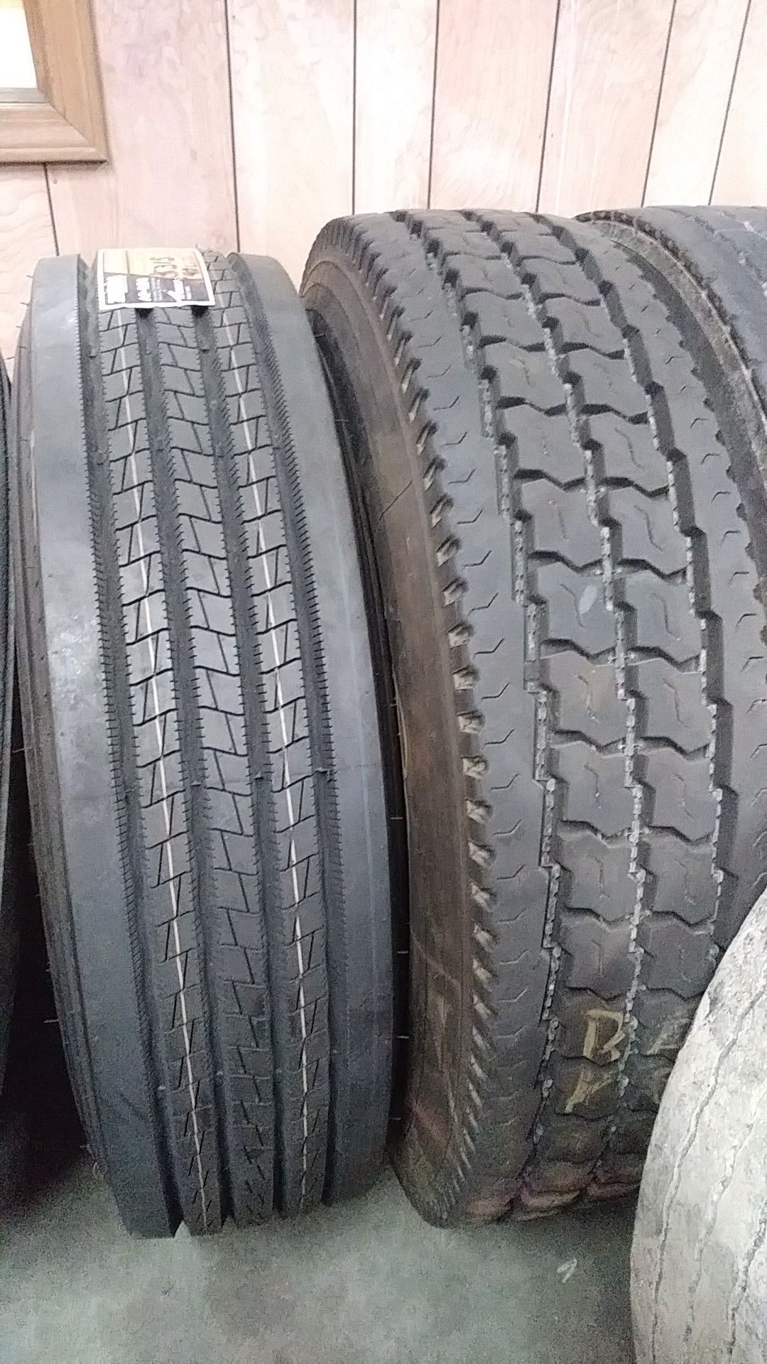 Two large black truck tires leaning against a wooden wall.