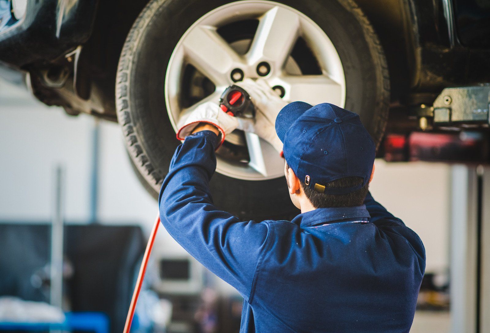 Mechanic in blue uniform uses a power tool on a car tire inside a repair shop.