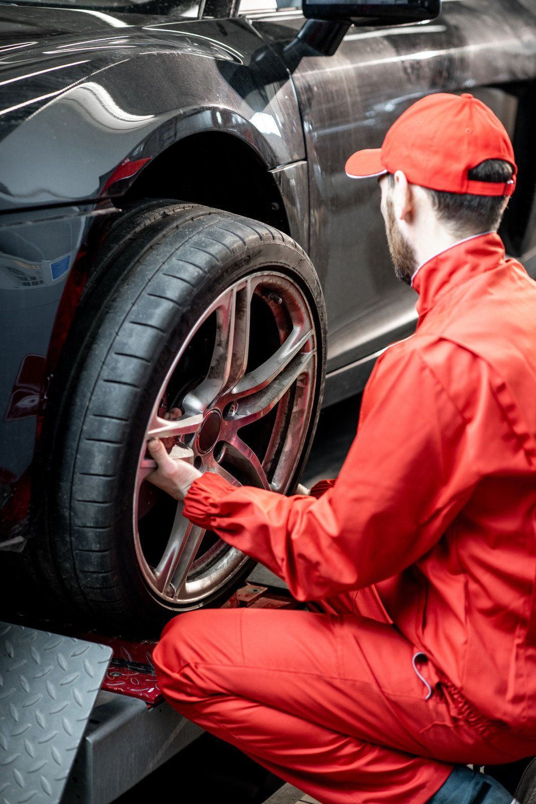 Mechanic in red overalls working on a car's tire, likely changing or checking it.